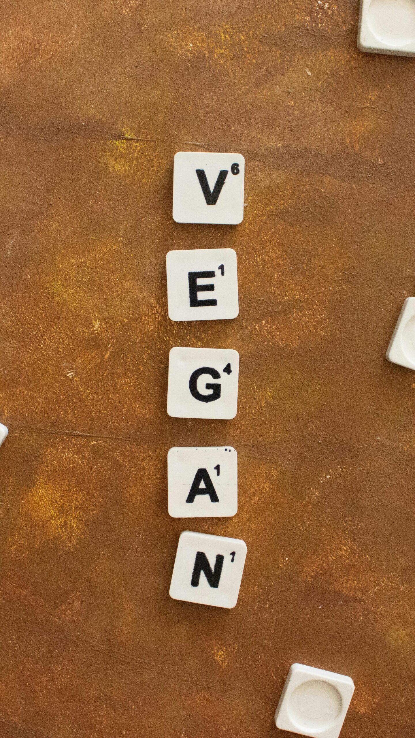 Flat lay of scattered scrabble tiles spelling 'VEGAN' on a rustic brown background.